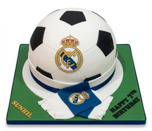 3D football cake with Real Madrid logo and edible scarf on a green board with custom message.