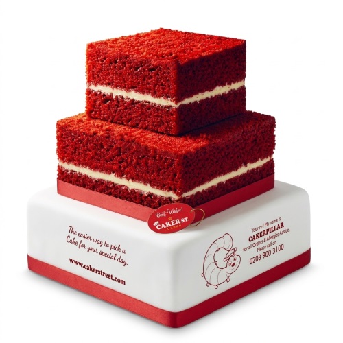 Two tier square red velvet style cake with white filling and red ribbon on a white base.