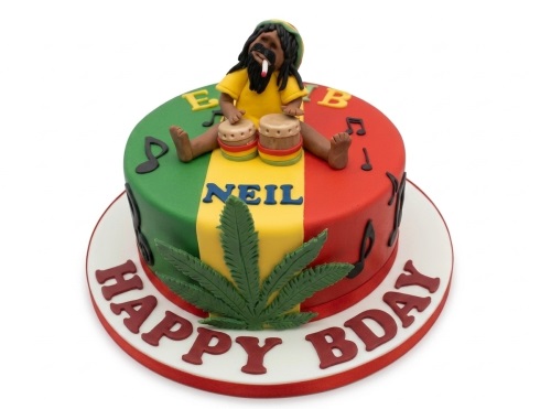 Round reggae theme birthday cake with Rasta colours, bongo player figure, music notes, and a cannabis leaf decoration.