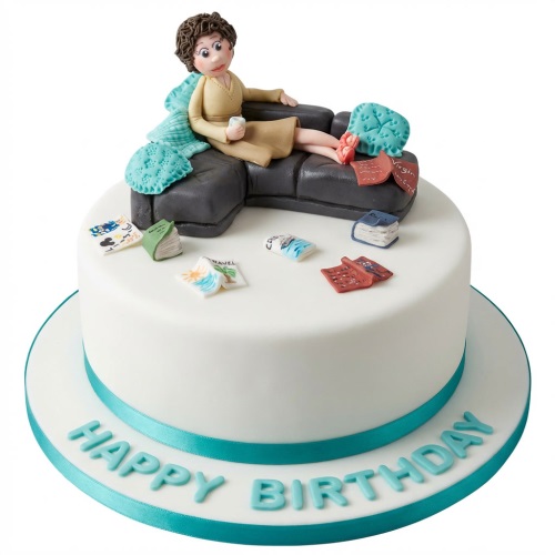 Round white birthday cake with a fondant woman on a sofa, books, and travel magazines.