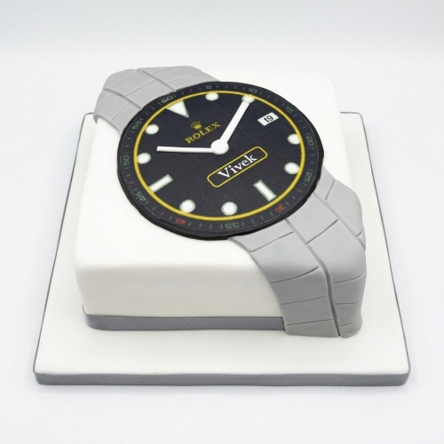 White square cake with an edible black Rolex watch face and grey strap.