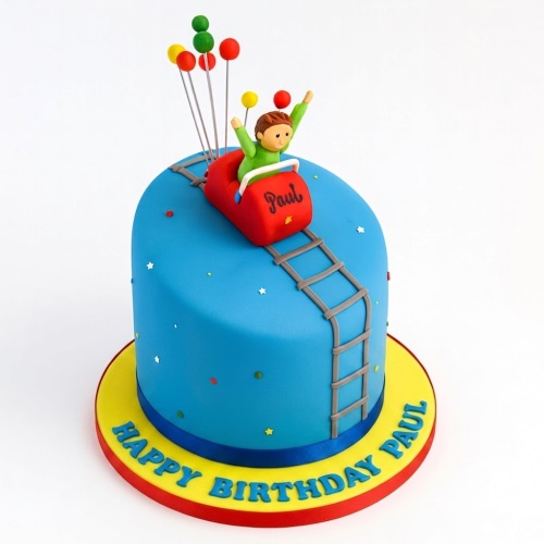 Blue round cake with a red rollercoaster car, a boy figure, and colourful balloons on top. A grey track goes up the side, and the cake board is yellow with a custom message.