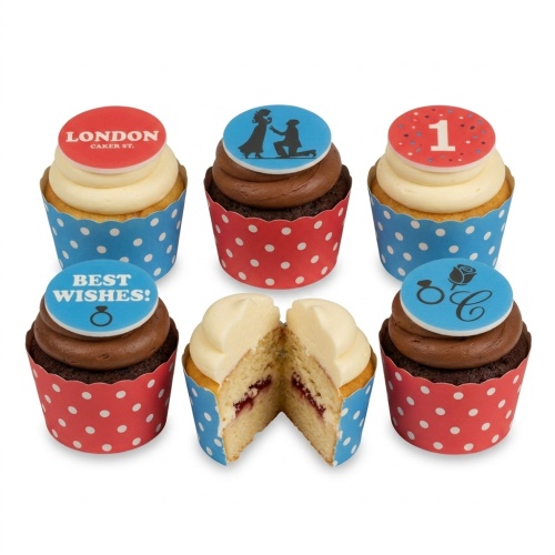 Six cupcakes with red and blue polka dot wrappers, topped with vanilla and chocolate frosting, featuring engagement and celebration themed edible discs including a proposal silhouette, rings, 'Best Wishes!', and a custom number '1'.