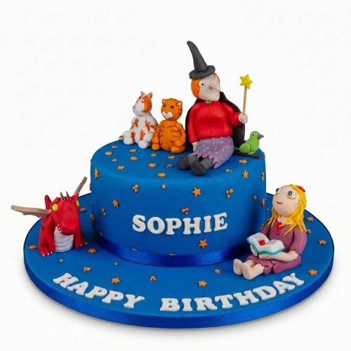 Blue round birthday cake with edible figures of a witch, dragon, cat, dog, bird, and a girl reading a book, with orange star sprinkles.