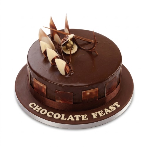 Round chocolate cake with glossy glaze, chocolate shards, white chocolate accents, and a golden ornament.