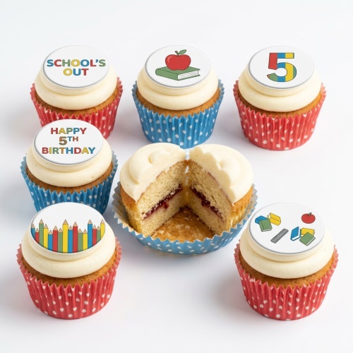 Vanilla cupcakes with white frosting and edible school-themed toppers, including apples, books, pencils, and a number 5.