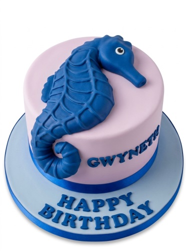 Round pink birthday cake with a large blue seahorse decoration and customisable 'Happy Birthday' message.