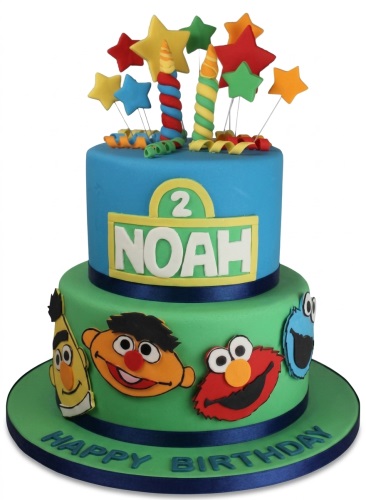 Two-tier blue and green Sesame Street themed birthday cake with star toppers, twisted candles, and character cutouts.