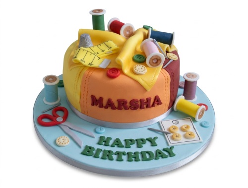 Round fondant cake decorated with edible sewing themed items like thread spools, buttons, scissors, and a measuring tape, with a personalised message.