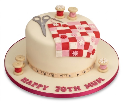 Cream round birthday cake with a quilt pattern, scissors, thread spools, and a measuring tape border. Custom message.