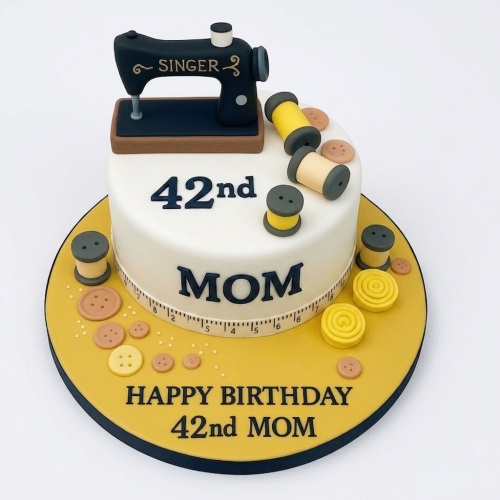 White round birthday cake with a black sewing machine, yellow thread spools, and brown buttons. Features a custom age and message.