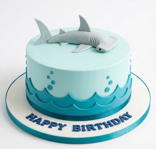 Round blue birthday cake with a grey hammerhead shark topper and blue wave decorations.