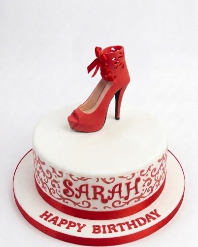 White round birthday cake with red high heel shoe topper, red scrollwork, and personalised message.