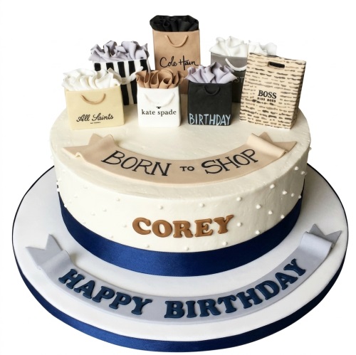 Round white birthday cake with navy ribbon, edible shopping bags, 'Born to Shop' and 'Happy Birthday' banners.