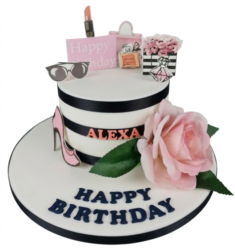Two-tier white fashion theme birthday cake with black ribbons, pink high heel, rose, lipstick, handbag, perfume, and sunglasses toppers.