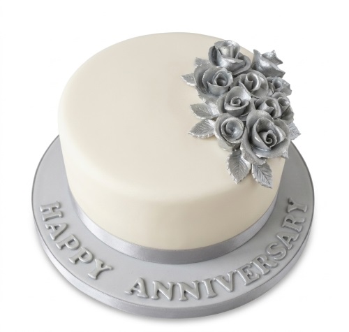 Round cream cake with silver sugar roses, silver ribbon, and "Happy Anniversary" text.