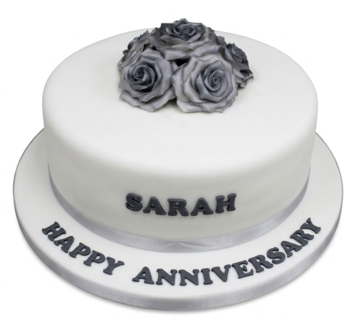White anniversary cake with silver roses and a silver ribbon, personalised with a message.