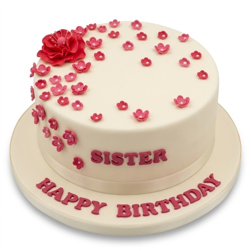 Round cream birthday cake with scattered pink and red sugar flowers, and a custom message.