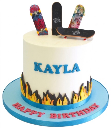 White round cake with miniature skateboards on top, flame decoration around the base, and a blue ribbon.
