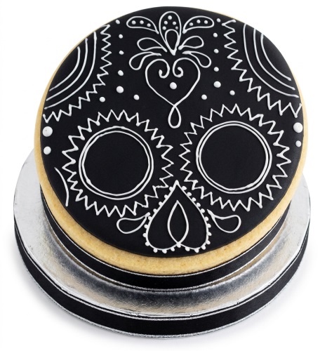 Round black cake with white sugar skull design and intricate piping on a silver cake board.