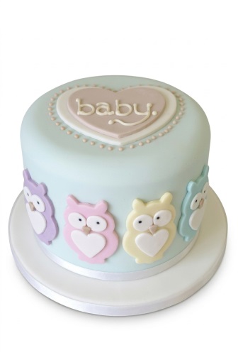 Round light blue cake with pastel owl decorations and a pink heart with "baby" on top.