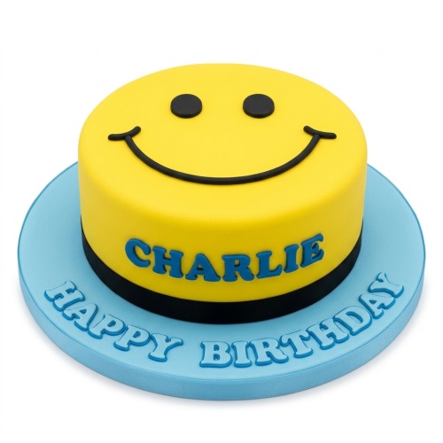 Round yellow cake with a black smiley face design on top, on a blue cake board with a custom name and 'Happy Birthday' message.