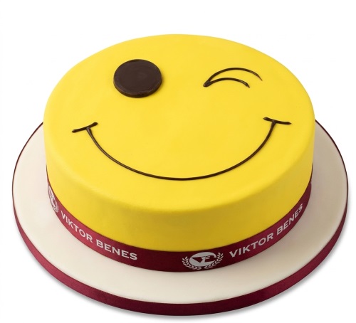 Round yellow winking smiley face birthday cake with a dark red ribbon.