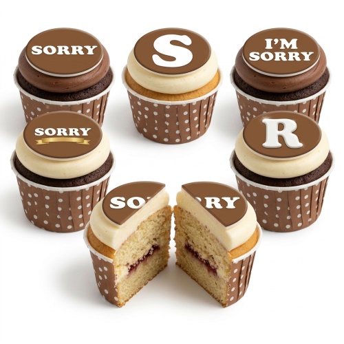 Six cupcakes with brown and white frosting, spelling "I'M SORRY" on round brown toppers. Some have chocolate sponge, others vanilla with jam filling.