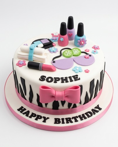 Round white cake with black zebra stripes, pink bow, and make-up decorations including nail polish, lipstick, and sunglasses. Personalised birthday cake.