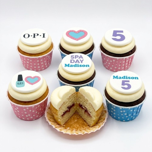 Assortment of vanilla and chocolate cupcakes with white frosting, topped with edible discs featuring OPI logo, hearts, a number 5, and "SPA DAY Madison" text.