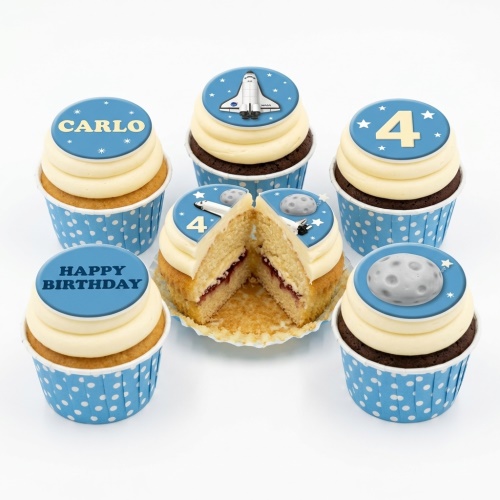 Space themed cupcakes with blue toppers, featuring a space shuttle, moon, and stars, with examples of custom age and name.