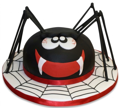 Black spider cake with red fangs and web design on a white cake board.