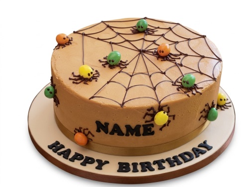Round tan birthday cake with a chocolate spiderweb on top and colourful yellow, green, and orange fondant spiders on the cake and board. Features a personalised name and 'Happy Birthday' message.