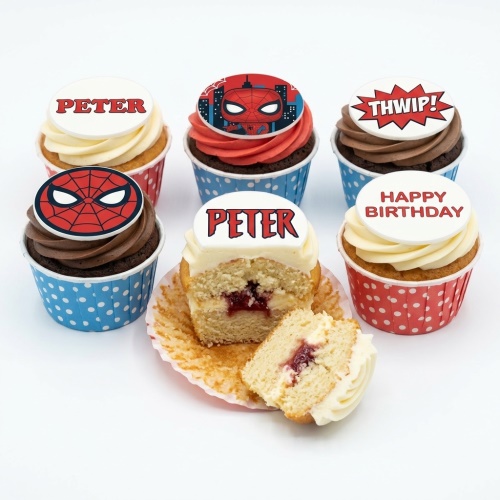 A selection of Spiderman themed cupcakes with red and blue wrappers, featuring Spiderman mask and comic sound effect toppers.