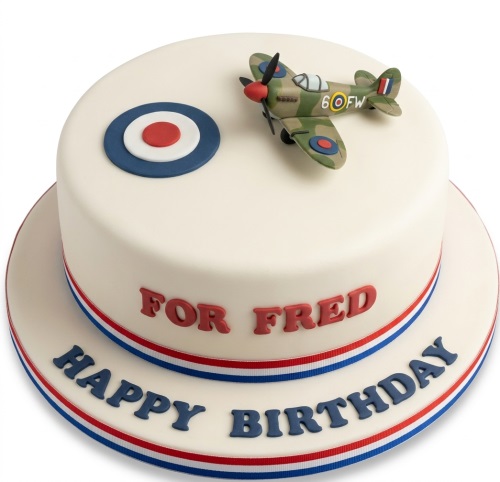 White single-tier birthday cake with a 3D Spitfire aeroplane model, RAF roundel, and red, white, and blue ribbon.