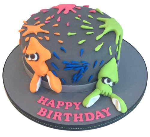 Round grey Splatoon-themed birthday cake with orange and green squid characters and colourful paint splatters.