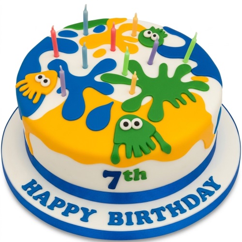 Round white birthday cake with blue, yellow, green paint splatters, cartoon blob characters, and colourful candles.