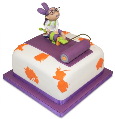 White square cake with purple ribbon, orange ink splatters, and a Splatoon-like character topper with a paint roller.