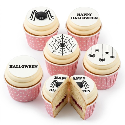 White cupcakes with vanilla frosting and black spider and spiderweb toppers, in pink polka dot wrappers, for Halloween.