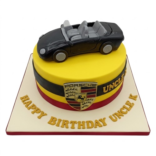 Round yellow birthday cake with a black convertible car topper and Porsche emblem.