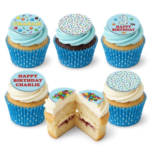Six birthday cupcakes with light blue and white frosting, blue polka dot wrappers, and edible toppers featuring M&M's candies, colourful sprinkles, and custom messages. One cupcake is cut open showing vanilla sponge with jam filling.