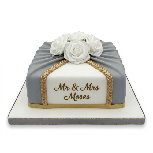 Rectangular elegant anniversary cake with white roses, grey draped fondant, and gold trim.