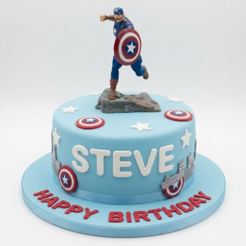 Round blue Captain America themed birthday cake with a superhero figure, shields, stars, and city skyline decorations.