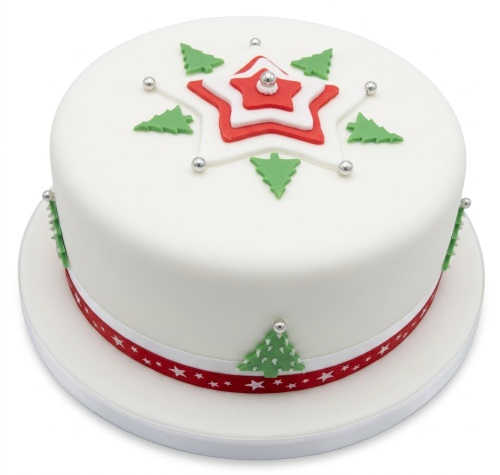 Round white Christmas cake with red star, green trees, and silver baubles.