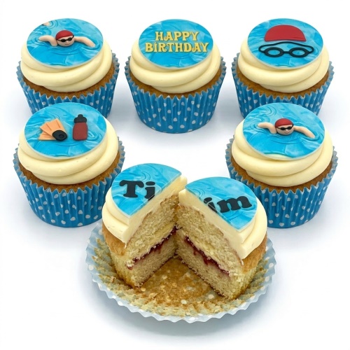 Six cupcakes with white frosting and blue swimming-themed edible toppers, including swimmers, goggles, and fins.
