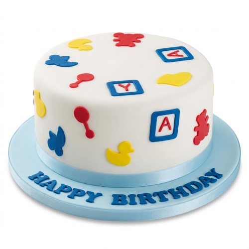Round white cake with colourful baby blocks, rattles, duck, and teddy bear decorations, on a blue board with "Happy Birthday".