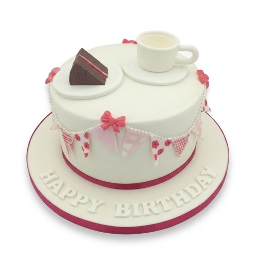 White round birthday cake with a miniature teacup, cake slice, and pink bunting decorations.