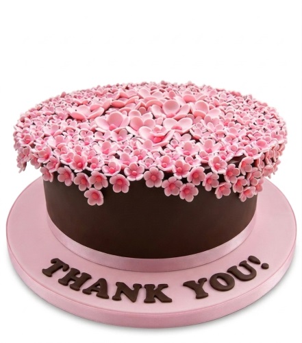 Round dark brown cake with pink sugar blossom flowers and a pink cake board with a custom message.