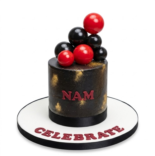 Single-tier black cake with gold speckles, topped with red and black glossy spheres, on a white board with a red 'CELEBRATE' message.
