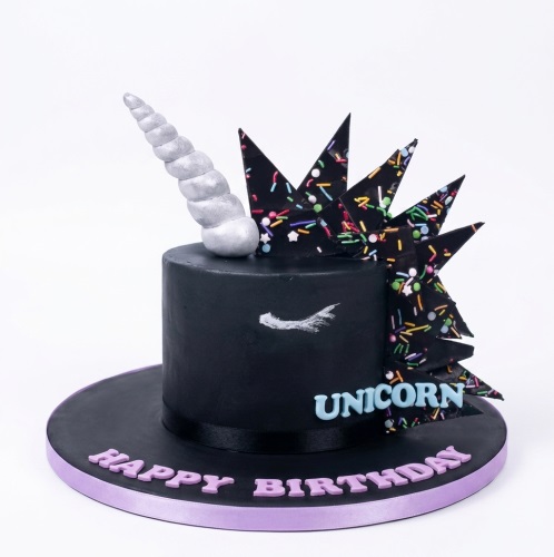 Black unicorn birthday cake with silver horn, sprinkle mane, and 'Happy Birthday' message.